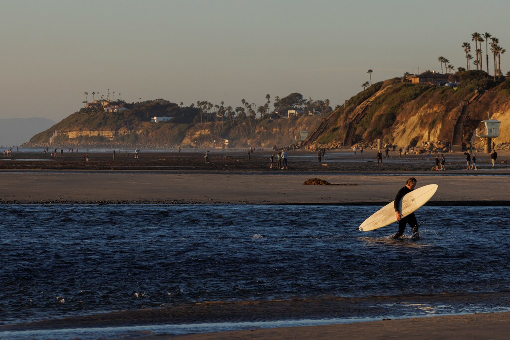 A longboard surfer walks out of the ocean during a very low tide at Cardiff State Beach in Encinitas, California, U.S., January 4, 2022. REUTERS/Mike Blake