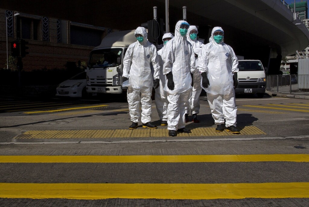 Health officers in full protective gear wait to cross a road near a wholesale poultry market in Hong Kong December 31, 2014.