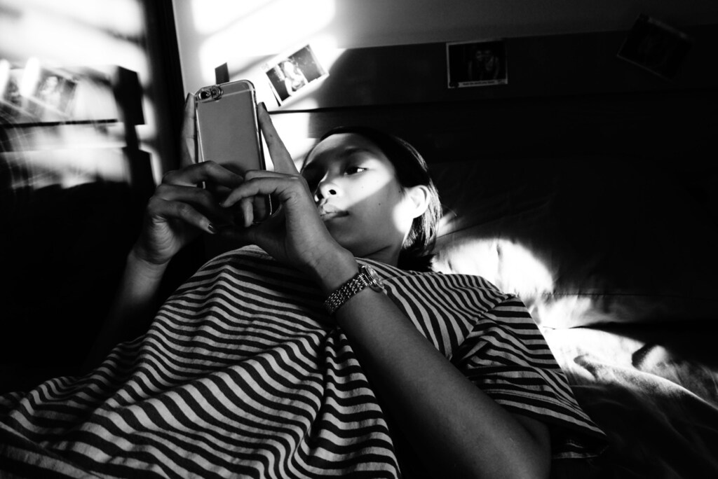 a woman lays on her bed whilst looking at a mobile phone in a black and white picture