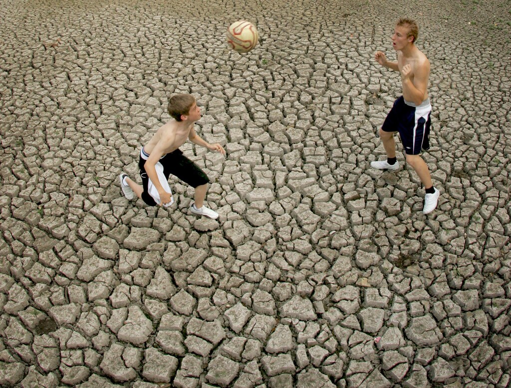Two young men play football on the dried up ground on West Common in Gerrard's Cross, southern England, July 26, 2006. Britain is currently experiencing a summer heatwave with record temperatures for July recently set and many water-use restrictions in place. REUTERS/Toby Melville (BRITAIN) - GM1DTDDPSQAA