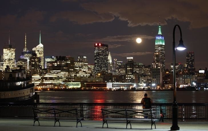 A full moon rises behind the Empire State Building in New York as a man watches in a park along the Hudson River in Hoboken, New Jersey, February 25, 2013. REUTERS/Gary Hershorn (UNITED STATES - Tags: CITYSCAPE)