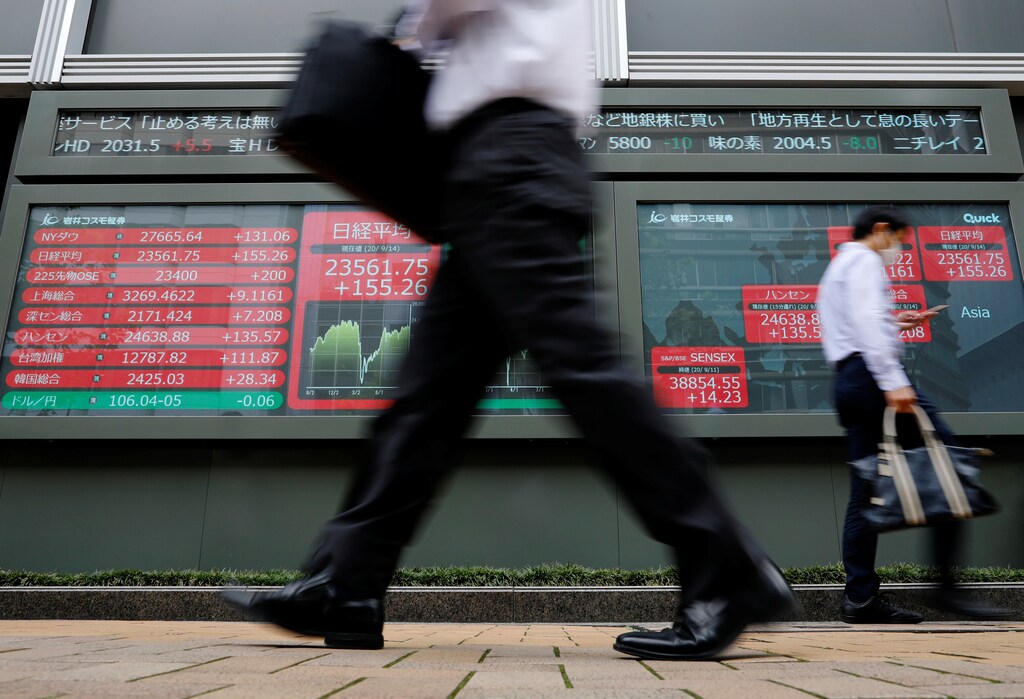 Passersby wearing protective masks walk past an electronic board showing Japan's Nikkei average, the exchange rate between Japanese yen against the U.S. dollar and other world's benchmarks outside a brokerage, amid the coronavirus disease (COVID-19) outbreak, in Tokyo, Japan September 14, 2020. REUTERS/Issei Kato - RC26YI9MI5WC
