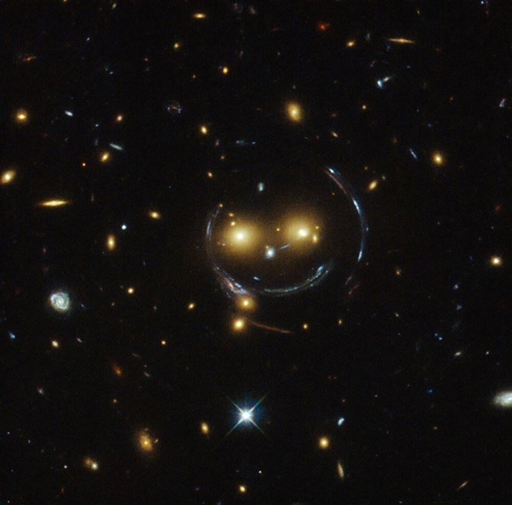 The galaxy cluster SDSS J1038+4849 is pictured in this undated handout image taken with the NASA/ESA Hubble Space Telescope. As a result of the phenomenon of gravitational lensing, it seems to be smiling. In the case of this "happy face"?, the two eyes are very bright galaxies and the smile lines are actually arcs caused by strong gravitational lensing. Galaxy clusters are the most massive structures in the Universe and exert such a powerful gravitational pull that they warp the spacetime around them and act as cosmic lenses which can magnify, distort and bend the light behind them. This phenomenon, crucial to many of Hubble's discoveries, can be explained by Einstein's theory of general relativity. REUTERS/NASA/Handout via Reuters (OUTER SPACE - Tags: SCIENCE TECHNOLOGY ENVIRONMENT) THIS IMAGE HAS BEEN SUPPLIED BY A THIRD PARTY. IT IS DISTRIBUTED, EXACTLY AS RECEIVED BY REUTERS, AS A SERVICE TO CLIENTS. FOR EDITORIAL USE ONLY. NOT FOR SALE FOR MARKETING OR ADVERTISING CAMPAIGNS - RTR4P1MQ