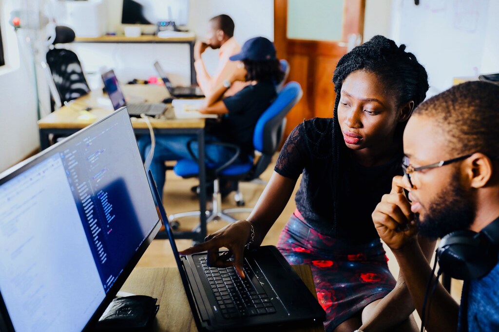 A woman working with a man in an office, at a computer.
