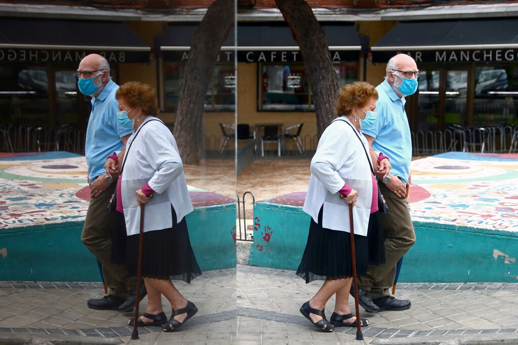 An elderly couple wearing protective face masks is reflected in a glass as they walk in the Usera neighbourhood during a partial lockdown between and within areas in six districts, amid the outbreak of the coronavirus disease (COVID-19), in Madrid, Spain September 23, 2020. REUTERS/Sergio Perez TPX IMAGES OF THE DAY - RC2A4J9M4JAB