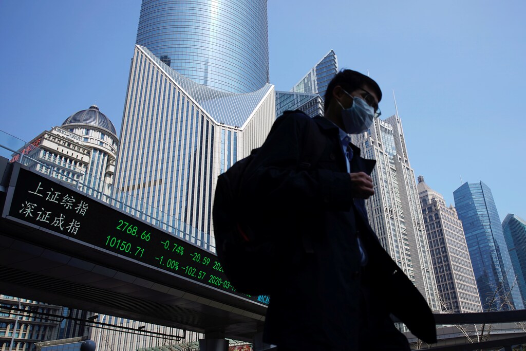 A pedestrian wearing a face mask walks near an overpass with an electronic board showing stock information, following an outbreak of the coronavirus disease (COVID-19), at Lujiazui financial district in Shanghai, China March 17, 2020. REUTERS/Aly Song - RC2FLF951HFT