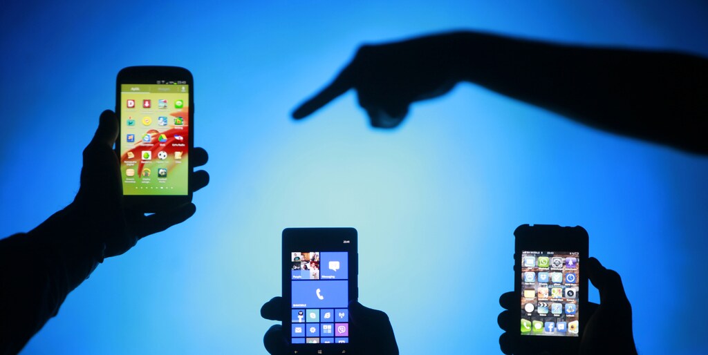 Men are silhouetted against a video screen as they pose with smartphones in the central Bosnian town of Zenica, May 17, 2013.