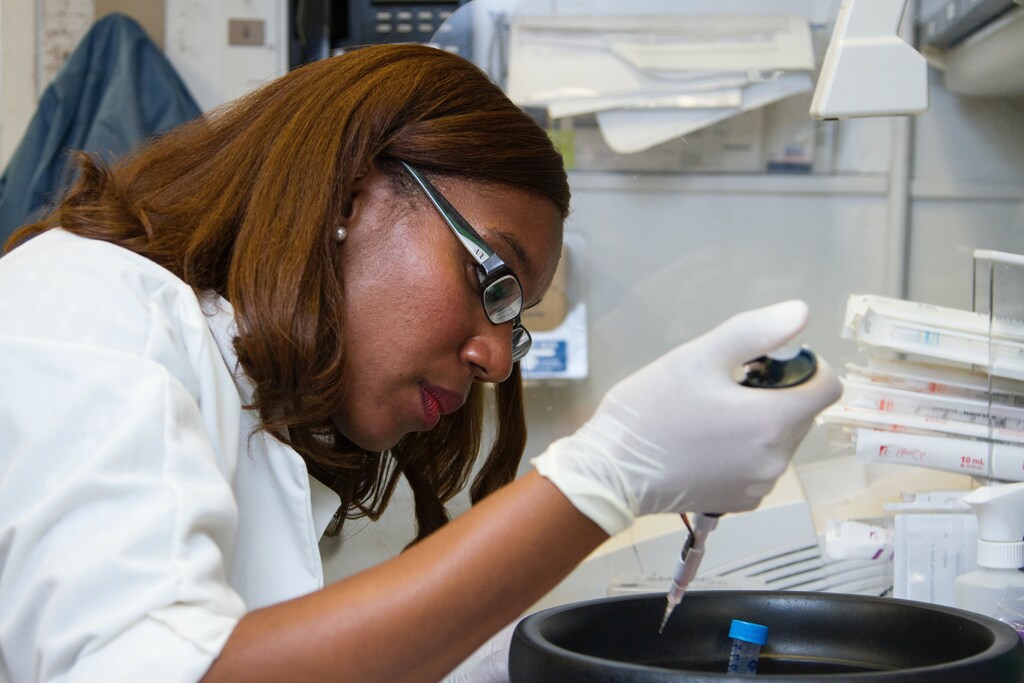 A woman wearing white pipetting samples into a tube.
