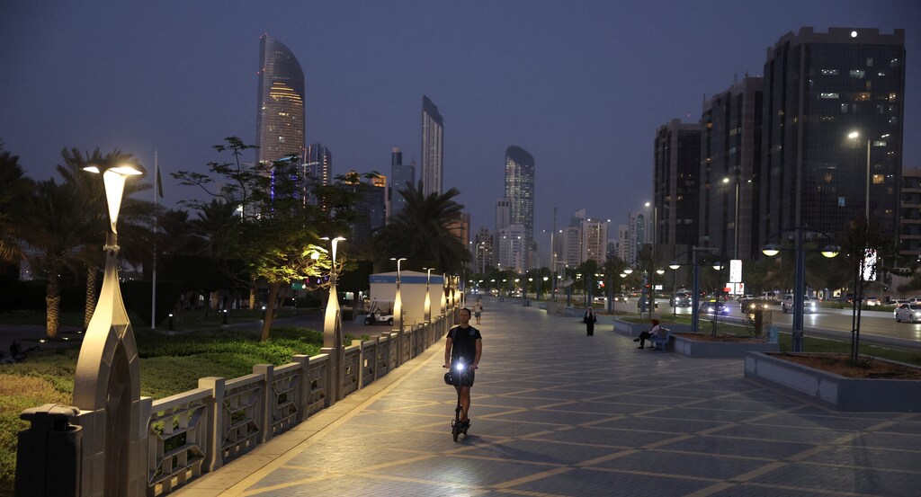 A person rides a scooter with the skyline visible in the background, in Abu Dhabi, United Arab Emirates, September 27, 2023. The Gulf states are working hard to build out their domestic non-oil economies.