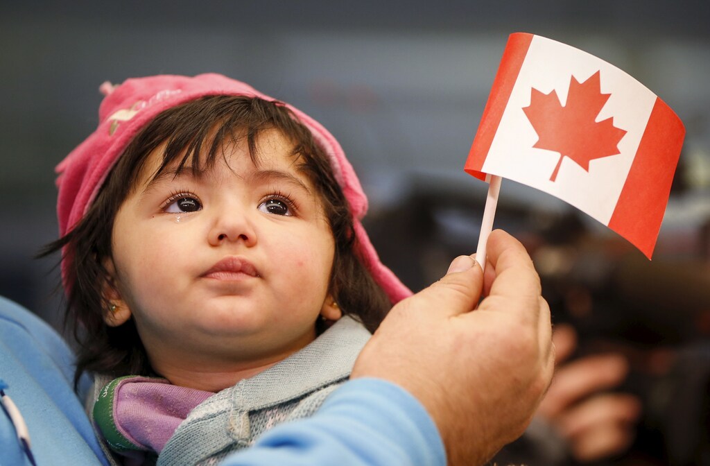 A Syrian refugee looks up as her father holds her and a Canadian flag as they arrive at Pearson Toronto International Airport in Mississauga, Ontario, December 18, 2015. REUTERS/Mark Blinch - GF10000270895