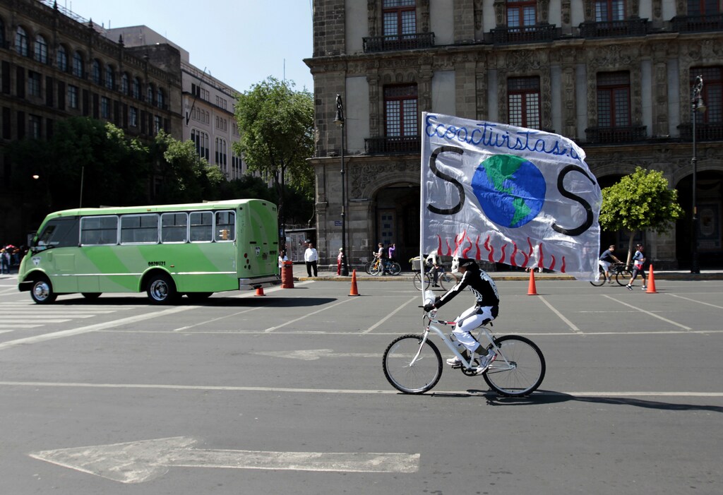 A man wearing a skull mask rides his bicycle as he carries a giant banner, reading "Ecotourists and a signal SOS ", at the main Zocalo square in Mexico City April 22, 2012. REUTERS/Henry Romero (MEXICO - Tags: SOCIETY) - RTR313GI
