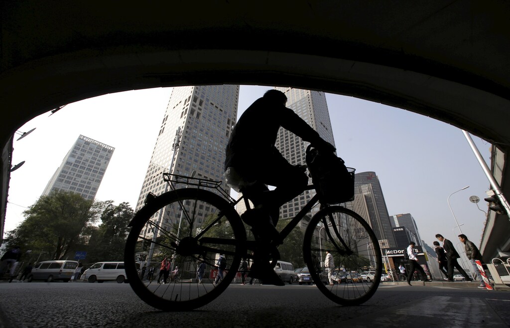 A man rides his bicycle across the street under the Guomao bridge at the Central Business District in Beijing, China, October 19, 2015. China posted its weakest quarterly economic growth since the global financial crisis on Monday, raising pressure on policymakers to cut interest rates further and roll out other support measures to avert a sharper slowdown. REUTERS/Jason Lee - RTS50W7