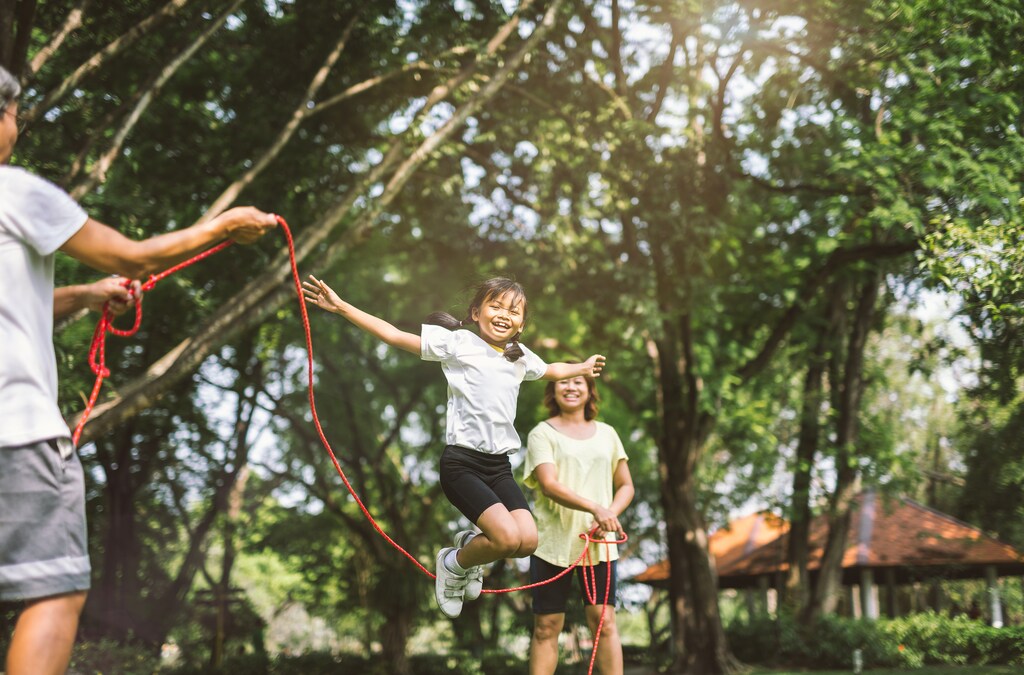 Summer vacation - happy family playing with skipping rope at green nature park