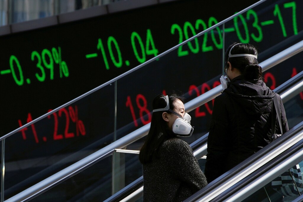 Pedestrians wearing protective masks ride an escalator near an overpass with an electronic board showing stock information, following an outbreak of the coronavirus disease (COVID-19), at Lujiazui financial district in Shanghai, China March 17, 2020. REUTERS/Aly Song - RC2ELF9N41H5