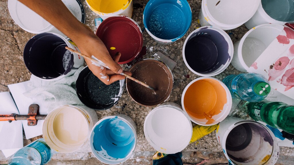 a birds eye view of different coloured paint pots with an artist reaching for one with a paintbrush