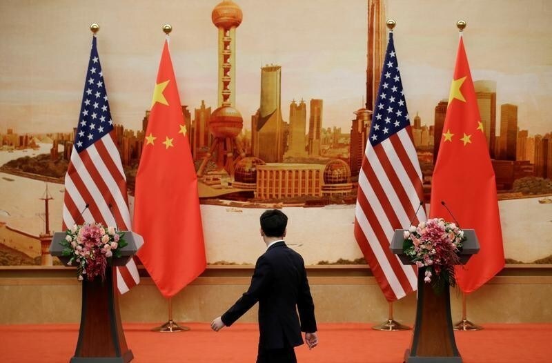 A staff member walks past U.S. and Chinese flags placed for a joint news conference by U.S. Secretary of State Mike Pompeo and Chinese Foreign Minister Wang Yi at the Great Hall of the People in Beijing, China June 14, 2018. REUTERS/Jason Lee - RC13AE41E700