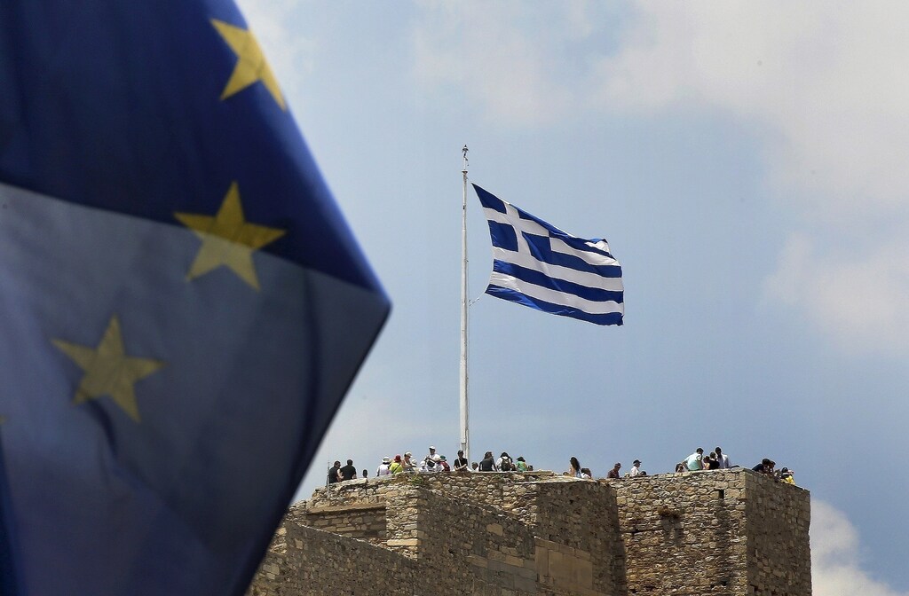 A European Union flag flutters as tourists gather around a Greek flag atop the Acropolis hill in Athens, Greece June 26, 2015. The leaders of Germany and France offered to release billions in frozen aid on Friday in a last-minute push to talk Greek Prime Minister Alexis Tsipras into contentious pension reforms in exchange for filling Athens' empty coffers until November.