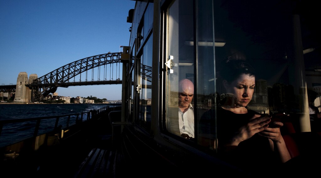 A commuter uses her mobile phone as a Circular Quay to Cockatoo Island ferry passes under the Sydney Harbour Bridge, November 24, 2015.