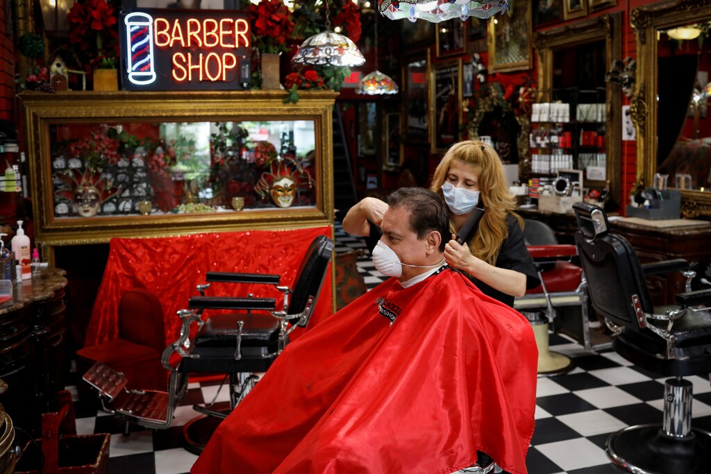 A hairdresser wearing a protective mask cuts the hair of a man at a barber shop, as Miami-Dade County eases some of the lockdown measures put in place during the coronavirus disease (COVID-19) outbreak, in Miami, Florida, U.S., May 18, 2020. REUTERS/Marco Bello - RC29RG9B5CG4