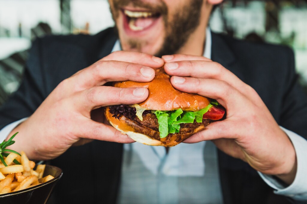 A picture of a man hold a big yummy burger about to bite into it, as a study reveals how we make food choices.