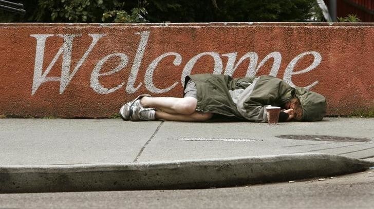 A homeless woman lies on a sidewalk using an empty coffee cup to collect spare change from passers-by in downtown Vancouver, British Columbia June 29, 2007. REUTERS/Andy Clark (CANADA)