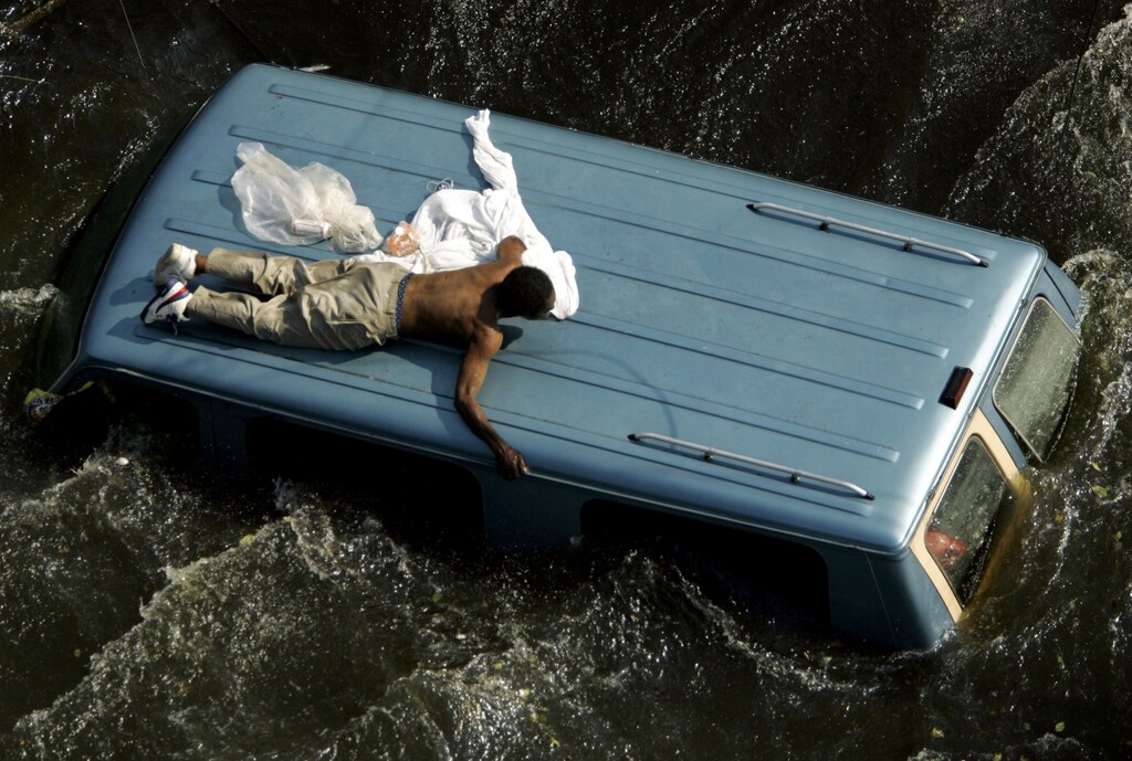 a man clings to the top of a vehicle before being rescued by the U.S. Coast Guard from the flooded streets of New Orleans, in the aftermath of Hurricane Katrina