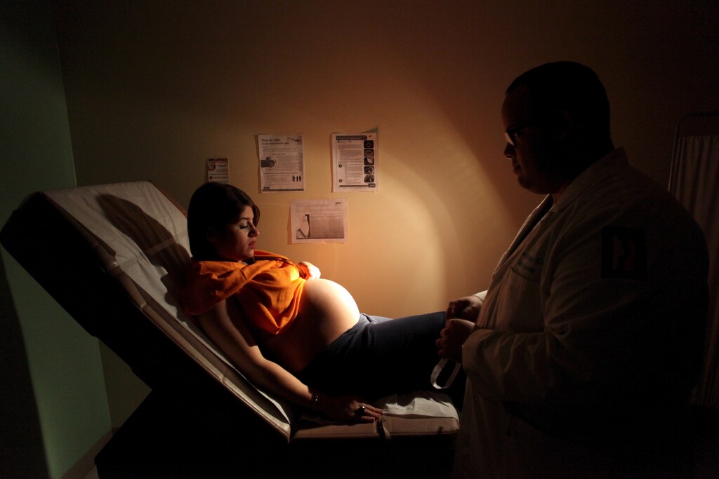 Noriany Rivera, who is 40 weeks pregnant, looks at her belly as she listens to a doctor during a routine check up, as fliers explaining how to prevent Zika, Dengue and Chikungunya viruses are posted on the wall, at a public hospital in San Juan, Puerto Rico, February 3, 2016. REUTERS/Alvin Baez - RTX25CBW