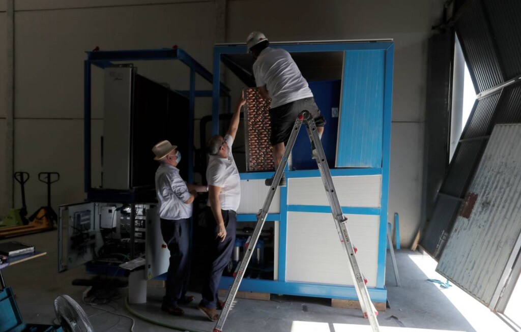 Spanish Aquaer company engineer and inventor, Enrique Veiga, 82, (L) and his son Juan (C), Aquaer CEO, check a machine which extracts drinking water from thin air before its first start-up, in Carrion de los Cespedes, near Seville, Spain, July 28, 2021.