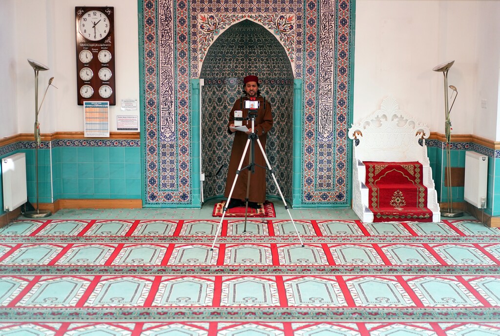 Imam Ajmal Masroor performs a Friday prayer service, broadcast online using his phone, at a mosque in north London.