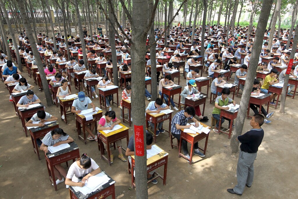 Students take term final exam among trees outside a classroom building at a middle school in Xinxiang, Henan province, China, July 3, 2015. The school set up the exam outdoor to create a more comfortable environment for the students, according to local media. Picture taken July 3, 2015. REUTERS/Stringer CHINA OUT. NO COMMERCIAL OR EDITORIAL SALES IN CHINA. - GF10000148188