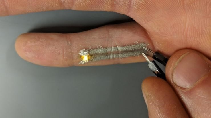 Two electronically active leads directly printed along the underside of Duke graduate student Nick Williams’s pinky successfully light up an LED when a voltage is applied.
