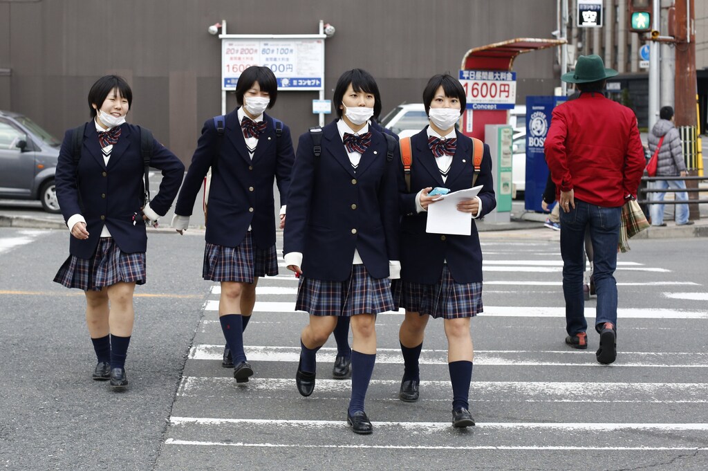 School girls, wearing surgical masks, cross a street at lunch time in Kyoto, western Japan November 19, 2014.