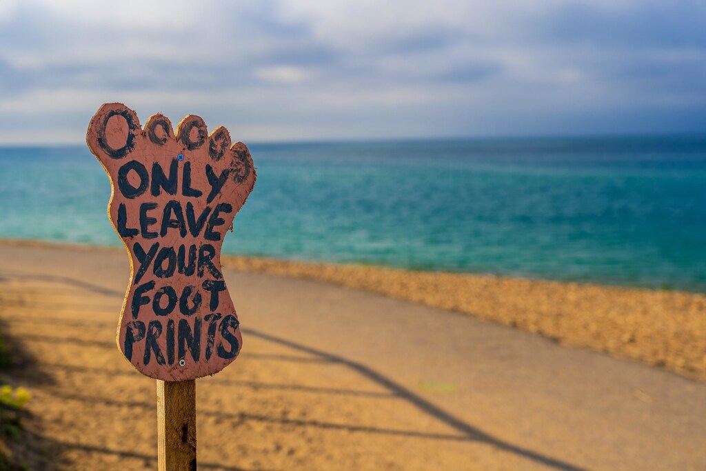 A beach with a sign that says leave only your footprints, indicating the need for sustainability