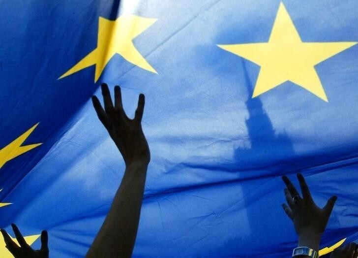People wave an European Union flag in front of the Palace of Culture during a EU parade in Warsaw May 15, 2005. A few hundred people marched through the Polish capital to celebrate European unity and express support for Ukraine's' EU ambitions before the Council of Europe Heads of State and Government Summit, held on May 16 and 17 in Warsaw. REUTERS/Katarina Stoltz PP05060270 PK/JOH
