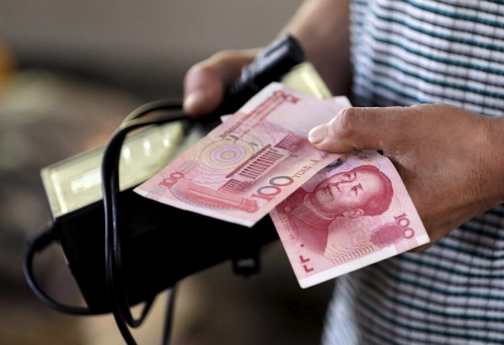 A customer holds a 100 Yuan note at a market in Beijing, August 12, 2015. China shocked global markets on Tuesday by devaluing its currency after a run of poor economic data, a move it billed as a free-market reform but which some experts suspect could be the beginning of a longer-term slide in the exchange rate.