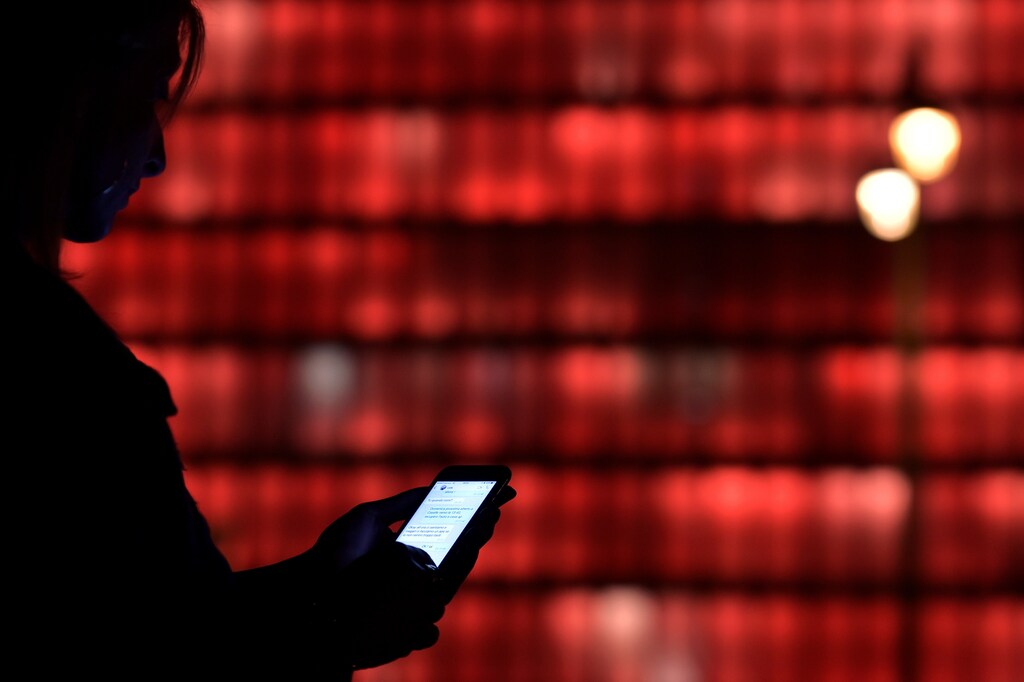 A woman holds a phone in front of an illuminated office in Brussels, Belgium August 13, 2017. REUTERS/Eric Vidal - RTS1BNXH