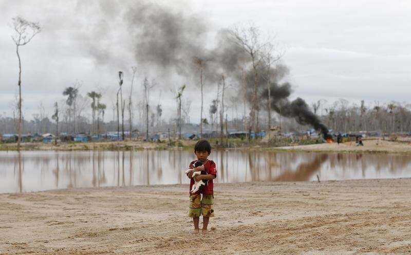 A boy carries a dog as he stands after a Peruvian police operation to destroy illegal gold mining camps in a zone known as Mega 14, in the southern Amazon region of Madre de Dios July 14, 2015. Peruvian police razed dozens of illegal gold mining camps at the edge of an Amazonian nature reserve this week, part of a renewed bid to halt the spread of wildcatting in a remote rainforest region. The stings at the edge of the Tambopata National Reserve were the first in the southeastern region of Madre de Dios since a crackdown let up in December. Production from wildcat miners in Madre de Dios, who sell their ore up the supply chain, made up about 10 percent of national production before President Ollanta Humala launched the harshest crackdown yet on illegal gold mining last year. Picture taken July 14, 2015. REUTERS/Janine Costa TPX IMAGES OF THE DAY - GF10000160480