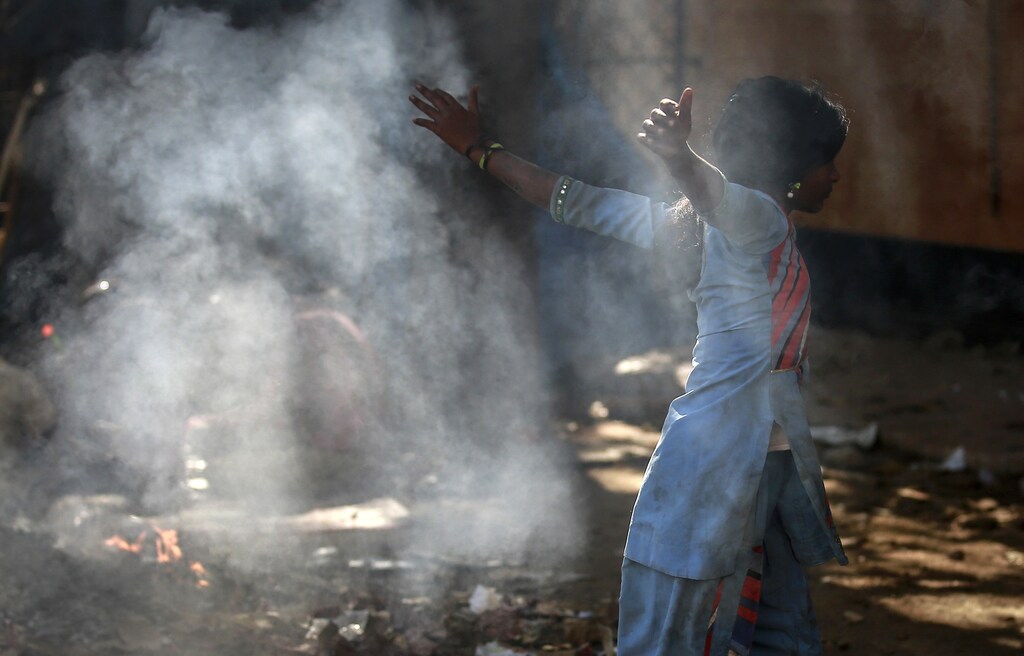 A girl plays amidst the smoke from the burning garbage outside a public toilet in Mumbai February 9, 2015. REUTERS/Danish Siddiqui (INDIA - Tags: SOCIETY POVERTY) - RTR4OUP2
