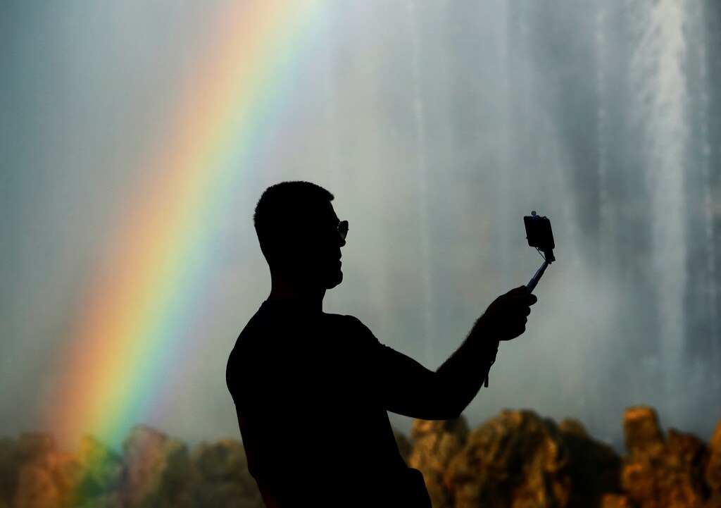 A man takes a selfie as a rainbow appears in the mist of a public fountain in Vienna, Austria, August 9, 2017. REUTERS/Heinz-Peter Bader - RC19D1E1F4A0