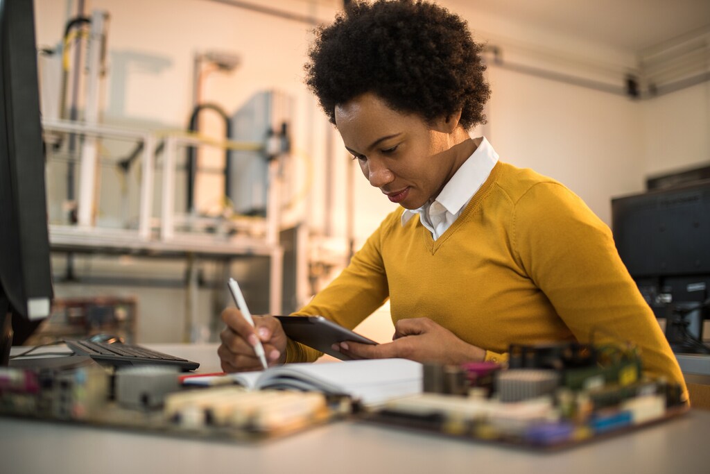 Black female engineer surfing the net on touchpad and writing while working in tech laboratory. Digital divide