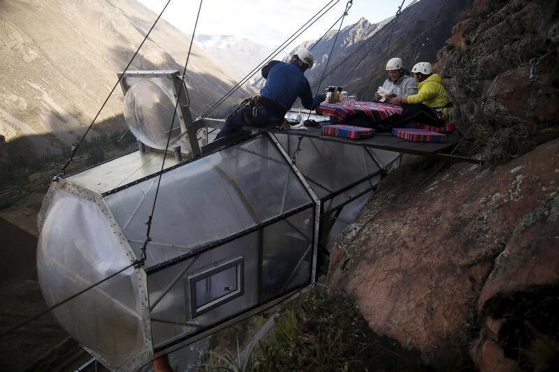 A guide (L) serves breakfast to guests above the cabine at the Skylodge Adventure Suites in the Sacred Valley in Cuzco, Peru, August 14, 2015. The Skylodge is composed by three capsule suites hanging at the top of the 1300 feet mountain with a 300 degree view of the Valley. To sleep at Skylodge, people must climb 400 meters of Via Ferrata path and to leave the hotel people go down a trail through ziplines.