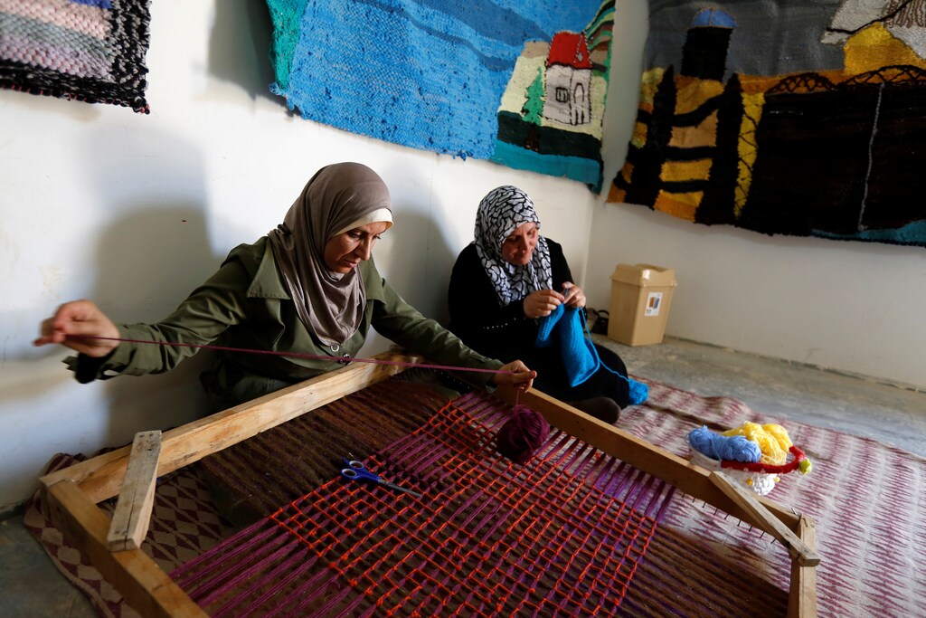A Syrian woman weaves wool as a colleague knits a baby shawl at a shelter for women built by the Italian NGO Building Peace Foundation and run by UN Women at Al Zaatari refugee camp outside Mafraq, Jordan.