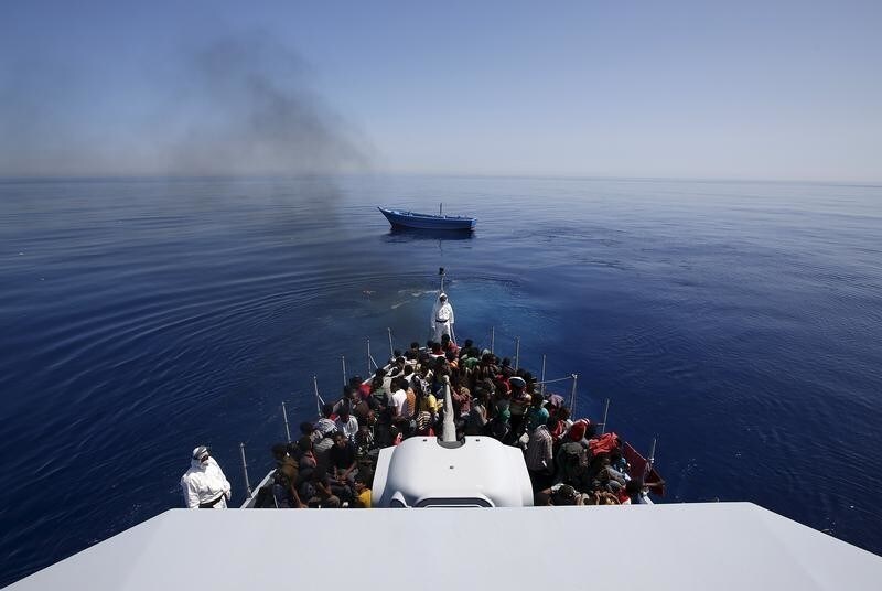 A group of 300 sub-Saharan Africans (bottom) sit on board the Italian Finance Police vessel Di Bartolo as their boat (Top) is left to adrift off the coast of Sicily, May 14, 2015. Around 1100 migrants were rescued off the coast of Sicily, about 130 miles from Lampedusa, according to the police.REUTERS/Alessandro Bianchi