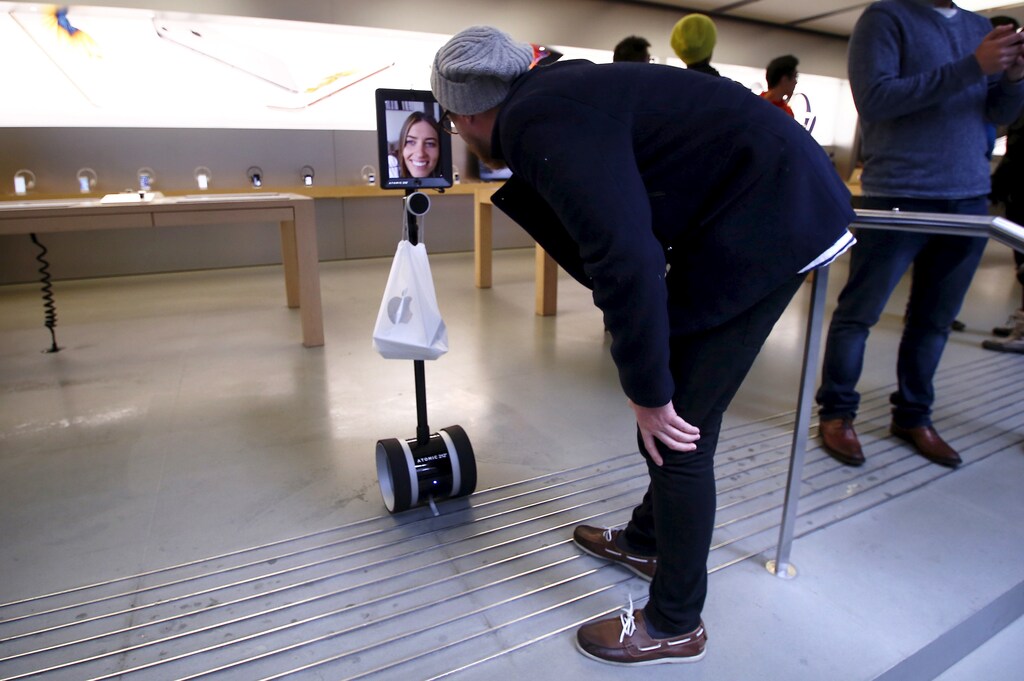 A man talks to Lucy Kelly on a screen attached to a 'telepresence robot', which she used to purchase her iPhone 6s during the official launch at the Apple store in central Sydney, Australia, September 25, 2015. The new iPhone 6s and 6s Plus arrive in stores and at consumers' doorsteps on Friday, kicking off a sales cycle that will be scrutinized for signs of how much juice Apple's marquee product has left. Apple has a tough act to follow after the success of the iPhone 6, but sales are expected to benefit this year from the inclusion of the Chinese market, where the gadget's debut was delayed in 2014 due to regulatory issues. REUTERS/David Gray - RTX1SCM3