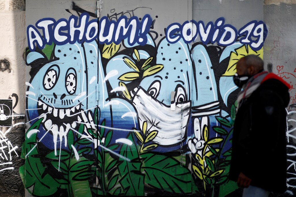 A man wearing a protective mask passes by a graffiti reading "Sneeze COVID-19" as a lockdown is imposed to slow down the coronavirus disease (COVID-19) spread in France, March 28, 2020. REUTERS/Benoit Tessier - RC20TF9EQ1W2