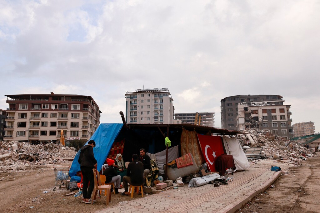 A family sits under a tent after their house collapsed due to the earthquake in Antakya, Hatay province, Turkey, February 21, 2023. REUTERS/Thaier Al-Sudani