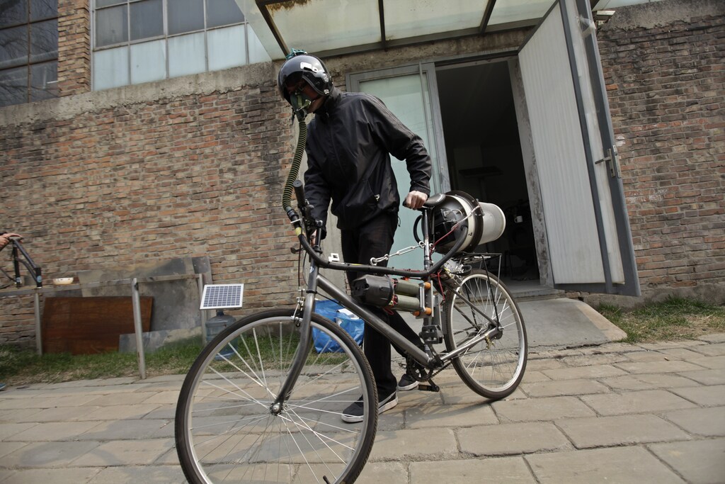 Artist Matt Hope, wearing a helmet, pushes his air filtration bike out from his studio on a hazy day in Beijing, March 26, 2013. Using an IKEA perforated garbage can, moped helmet, fighter-pilot breathing mask, wheel-powered generator and home air filtration system, Beijing-based artist Matt Hope built a "breathing bicycle" as a way of protecting himself from air pollution. While pedalling, electricity is generated for the power to activate the system to filter out haze and provide the rider with clean air, local media reported. According to the U.S. embassy monitor, the air quality today is classified as "very unhealthy". REUTERS/Petar Kujundzic (CHINA - Tags: ENVIRONMENT SOCIETY POLITICS TPX IMAGES OF THE DAY) - RTXXXRW