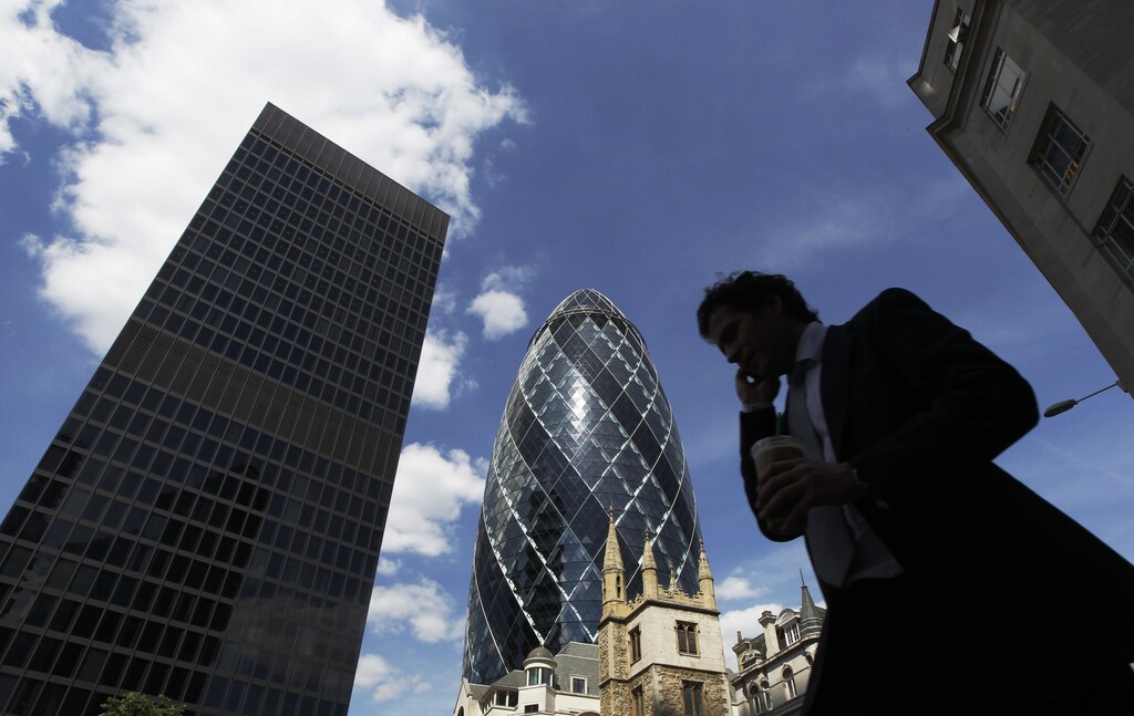 A man passes the Swiss RE building, also known as the Gherkin, in the financial district City of London June 22, 2010. Britain's Chancellor of the Exchequer George Osborne announced the harshest budget in a generation on Tuesday, promising to bring a record budget deficit of 11 percent of GDP down to 1 percent in 5 years. REUTERS/Luke MacGregor (BRITAIN - Tags: BUSINESS POLITICS) - LM1E66M17EI01
