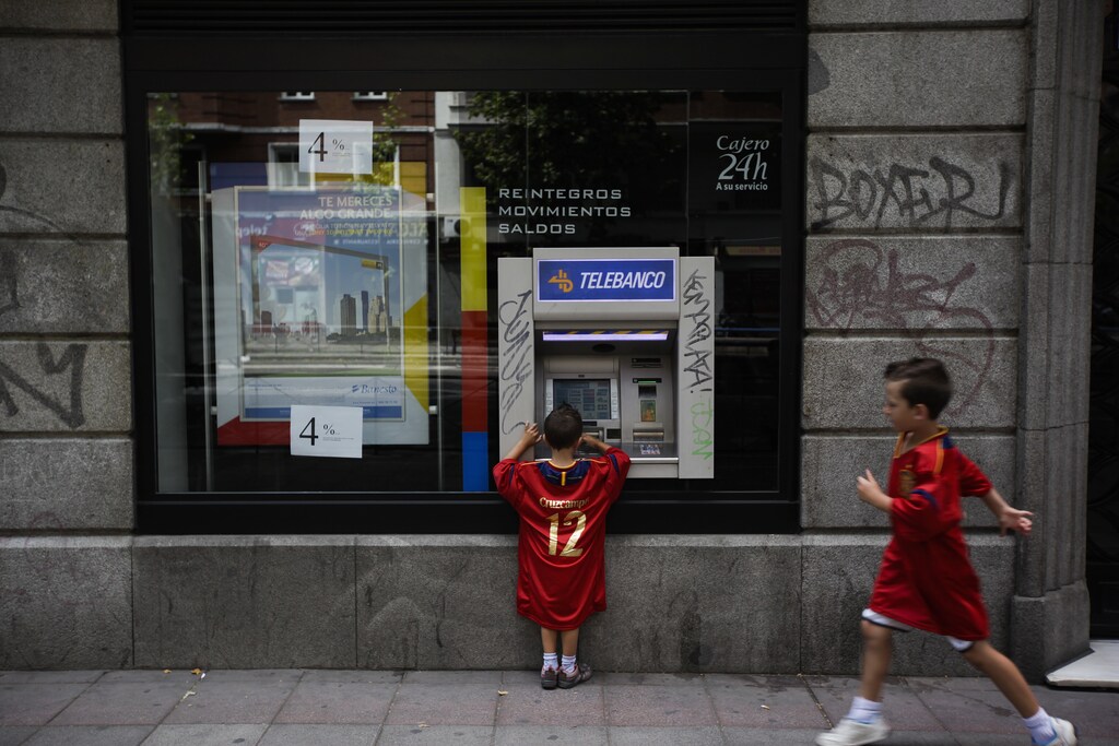 German Herrero Sanjuan, 9, approaches his brother Fernando, 5, as he plays with a Banesto bank ATM machine in Madrid July 1, 2012. They are both wearing Spanish national soccer team jerseys to show support for their team ahead the Euro 2012 final soccer match between Spain and Italy tonight. REUTERS/Susana Vera (SPAIN - Tags: SPORT SOCCER) - GM1E8711KJR01