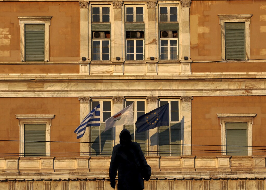 A woman is silhouetted against the parliament where the flags of Greece, Cyprus and the EU are fluttering in Athens, Greece June 24, 2015. Prime Minister Alexis Tsipras flew to Brussels to meet Greece's international creditors on Wednesday to try to bridge gaps on key elements of the proposals made by his left-wing government to shore up state finances in return for vital loans. REUTERS/Yannis Behrakis - RTR4YT1E